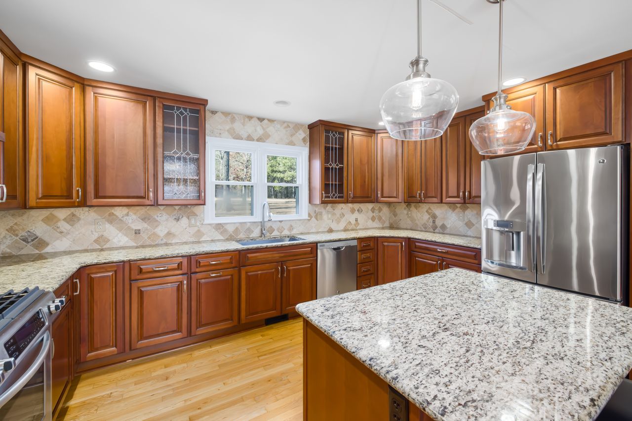 about-us-02 Spacious kitchen with wooden cabinets, granite island, and stainless steel appliances.