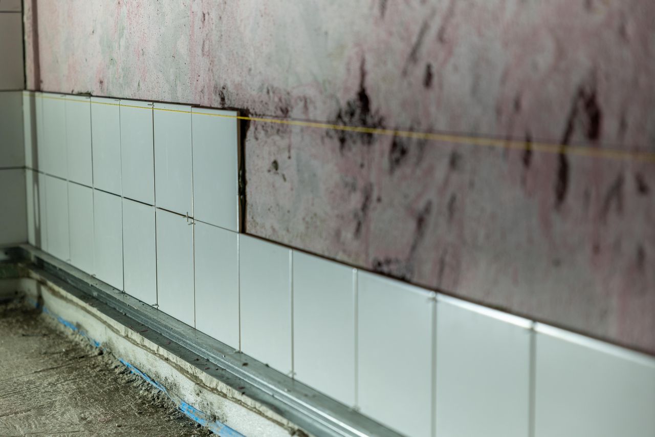 about-us-01 Close-up of partially tiled wall in a construction area, showcasing incomplete renovation work.