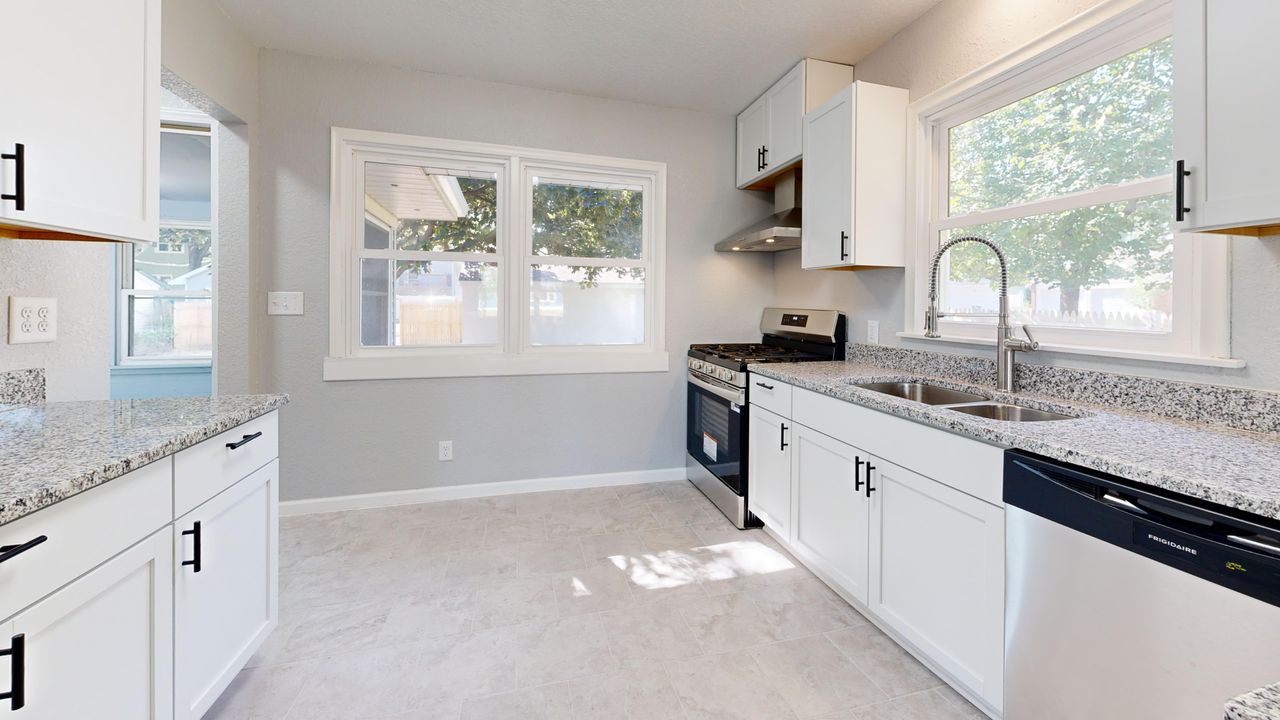 services-01 Sunlit modern kitchen featuring granite countertops and sleek white cabinetry.
